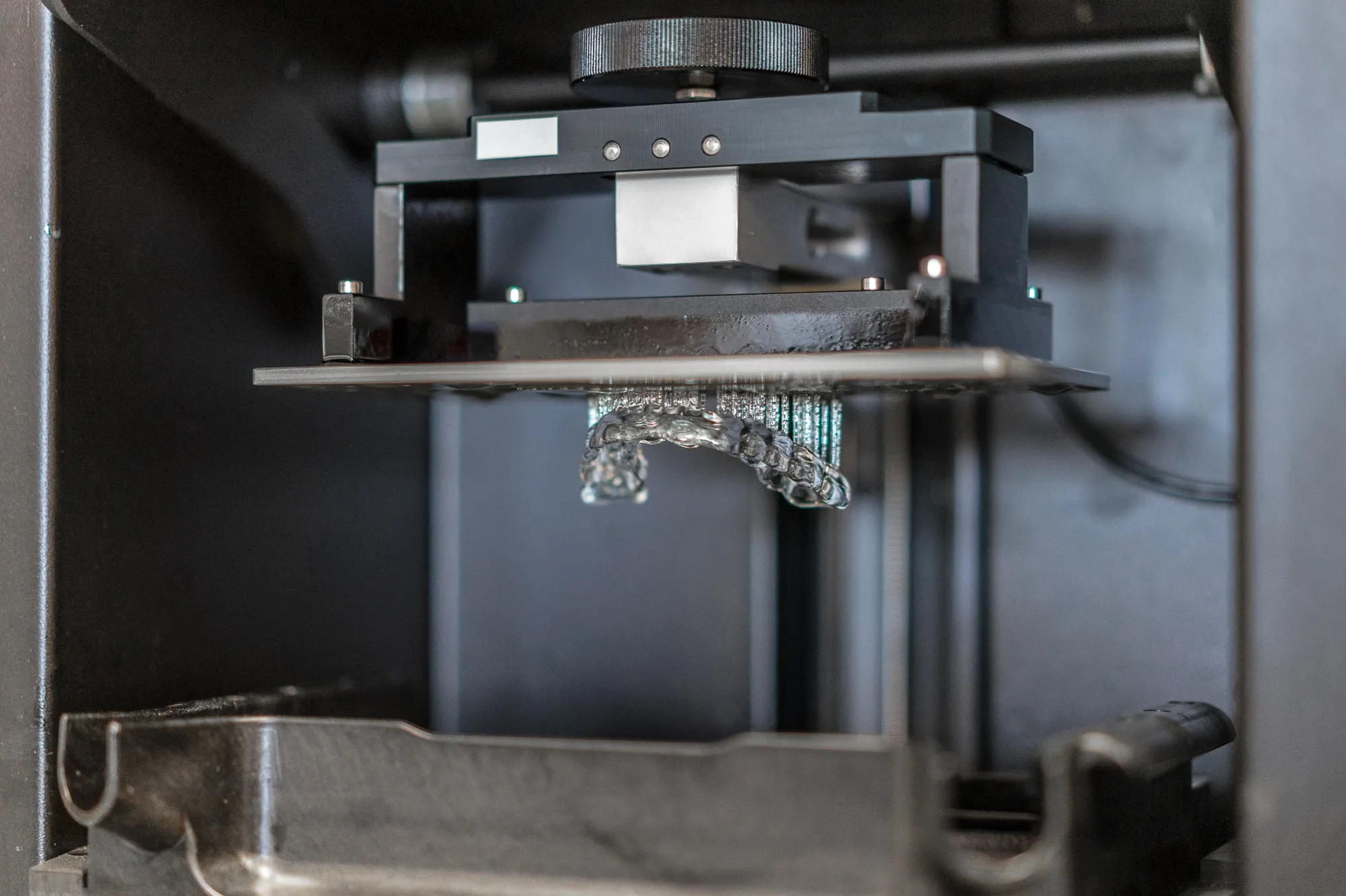 Makroaufnahme eines Dental-3D-Druckers: transparentes Werkstück wächst aus dem Resin vor schwarzem Hintergrund